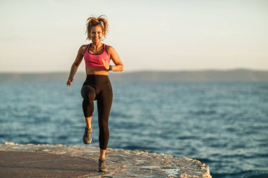 Mutlu genç bayan koşucu deniz kıyısındaki eğitim sırasında ısınma egzersizleri yapıyor..
