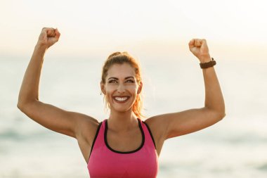 Genç ve zinde bir kadın kollarını kaldırarak kutluyor ve denize yakın egzersiz yaptıktan sonra dinleniyor..