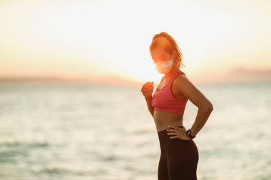 Deniz kıyısında antrenmana hazırlanırken koruyucu maske takan genç bir bayan koşucu..