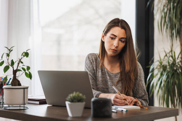 Young female entrepreneur looking thoughtful while working from her home office.