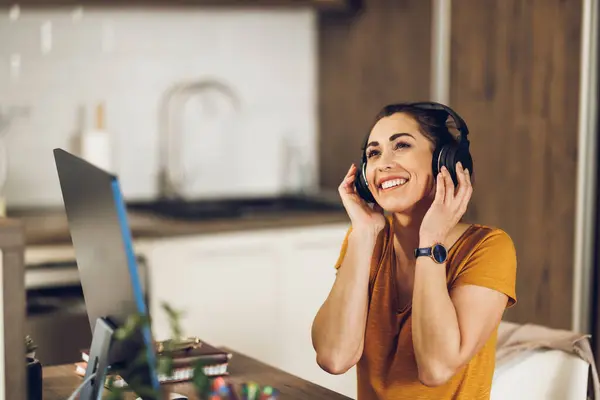 自宅で働くヘッドフォンが付いている肯定的な幸せな女性のフリーランスデザイナー — ストック写真