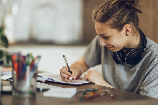 A beautiful teenage girl studying from home, writing in her notebook while learning at home.