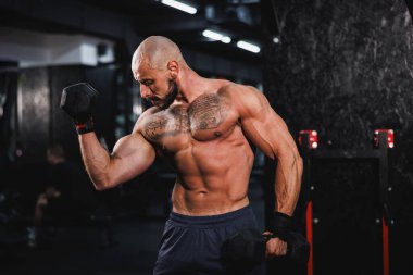 Spor salonunda dambılla ağır antrenman yapan kaslı bir vücut geliştiriciyi vurmuşlar. Pazularını ağırlıkla şişiriyor..