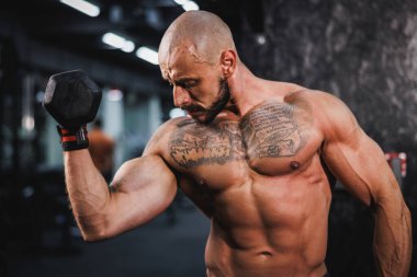 Spor salonunda dambılla ağır antrenman yapan kaslı bir vücut geliştiriciyi vurmuşlar. Pazularını ağırlıkla şişiriyor..