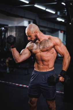 Spor salonunda dambılla ağır antrenman yapan kaslı bir vücut geliştiriciyi vurmuşlar. Pazularını ağırlıkla şişiriyor..