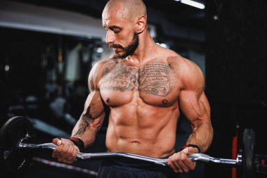 Kas geliştiren bir vücutçunun, spor salonunda kol kasları için halterle sıkı antrenman yaparken çekilmiş bir fotoğrafı..