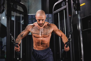 Genç, kaslı bir fitness adamı spor makinesinde göğüs kasları için sıkı antrenman yapıyor..