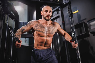 Genç kaslı bir vücut geliştiriciyi spor makinesinde göğüs kasları için sıkı antrenman yaparken çekmişler..