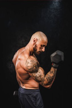 Spor salonunda dambılla sıkı antrenman yapan kaslı bir fitness oyuncusunun fotoğrafı. Pazularını ağırlıkla şişiriyor..