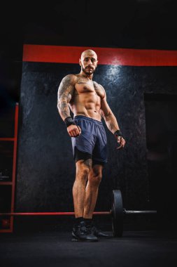 Spor salonunda egzersiz yaptıktan sonra mükemmel kaslarını gösteren genç kaslı bir vücut geliştirici. Kameraya bakıyorum..