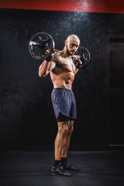 Spor salonunda omuz kasları için halterle sıkı antrenman yapan kaslı bir vücut geliştiriciyi vurmuşlar..