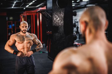 Spor salonunda idman yaptıktan sonra mükemmel kaslarını ayna önünde gösteren genç kaslı bir vücut geliştirici..