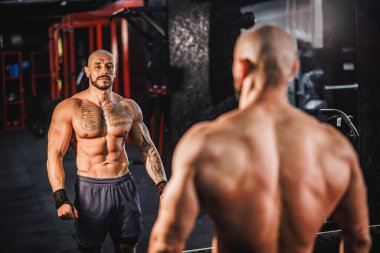 Genç bir fitness oyuncusunun mükemmel kaslı vücudunu ve altılı birasını spor salonunda aynanın önünde göstermesi..