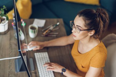 Genç bayan tasarımcı ev ofisinden bilgisayarla uğraşırken düşünceli görünüyor..