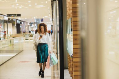 Alışveriş merkezinde alışveriş yaparken akıllı telefonunu kullanan genç bir kadının fotoğrafı..