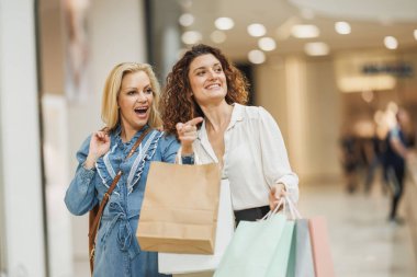 Çekici bir kadının, alışveriş merkezinde alışveriş yaparken en iyi arkadaşıyla yürürken bir şeyi işaret etmesi..