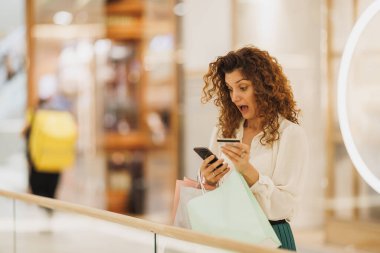 Kara Cuma ya da Siber Pazartesi satışları sırasında akıllı telefonuyla alışveriş merkezinde kart ödemesi yapan şaşırmış bir kadının fotoğrafı..