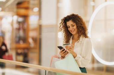 Mutlu bir kadının portresi akıllı telefonuyla Kara Cuma ya da Siber Pazartesi satışları sırasında bir alışveriş merkezinde kart ödemesi yapıyor..