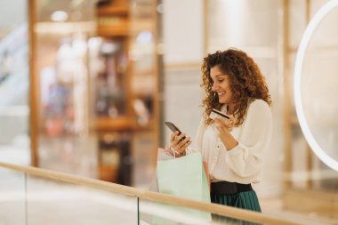 Kara Cuma ya da Siber Pazartesi satışları sırasında alışveriş merkezinde alışveriş yaparken akıllı telefonunu kullanan bir kadının fotoğrafı..