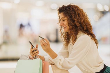 Çok mutlu alışveriş yapan bir kadının portresi Kara Cuma ya da Siber Pazartesi satışları sırasında akıllı telefonuyla kart ödemeleri yapıyor..