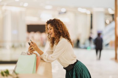 Genç bir kadının akıllı telefonuyla alışveriş merkezindeki mobil uygulamayı büyük satışlar sırasında kullanması..
