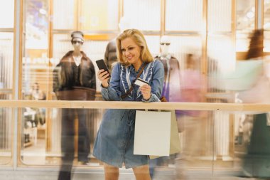 Gülümseyen bir kadının akıllı telefonunu ecommerce mobil uygulamasında alışverişin keyfini çıkarırken görüntüsü..