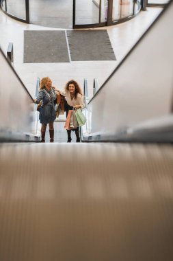 Alışveriş merkezinde eğlenen ve yürüyen merdivende dikilen iki çekici genç kadının çekimi. Alışveriş çılgınlığı sırasında..