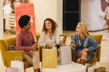 Üç çekici, gülümseyen kadının alışveriş merkezinde birlikte oturup eğlendiği bir fotoğraf..