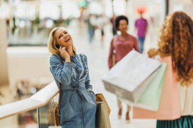 Kara Cuma ya da Siber Pazartesi satışları sırasında alışveriş merkezinde alışveriş yaparken akıllı telefondan konuşan neşeli kadın..