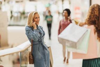 Kara Cuma ya da Siber Pazartesi satışları sırasında alışveriş merkezinde alışveriş yaparken akıllı telefonuyla konuşan mutlu kadın alışverişi..
