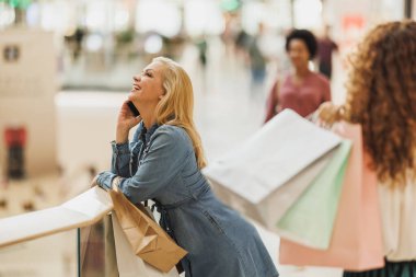 Alışveriş merkezinde alışveriş yaparken cep telefonu kullanan şık, neşeli bir kadın..