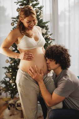 Genç adam Noel zamanı hamile karısının karnını öpüyor..