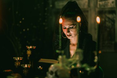 Yaratıcı karnaval kostümü giymiş çekici olgun bir kadın Cadılar Bayramı partisi için kocaman eski bir kitap okuyor..