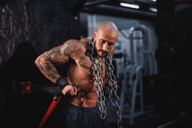 Genç bir fitness oyuncusunun boynunda ağır bir zincirle spor salonunda antrenman yapmaya hazırlanması..