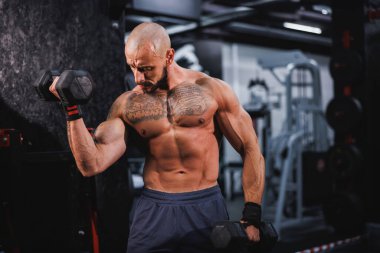 Spor salonunda dambılla ağır antrenman yapan kaslı bir vücut geliştiriciyi vurmuşlar. Pazularını ağırlıkla şişiriyor..
