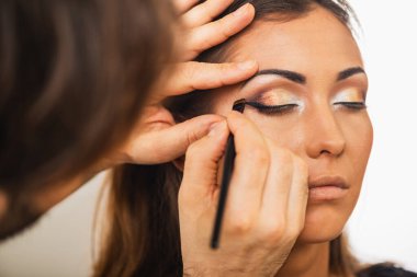 Güzel bir genç kadına göz kalemi çeken bir makyözün yakın çekimi..