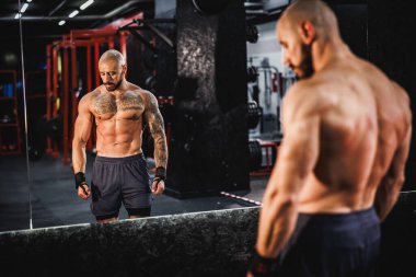 Genç kaslı bir vücut geliştiricinin mükemmel kaslarını jimnastik salonunda aynanın önünde göstermesi..