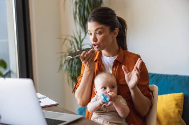 Anne, kızına bakıcılık yaparken ve evde çalışırken telefonda konuşmakla meşgul..