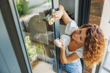 Gülümseyen kadın bir apartman dairesinde, evde ya da otelde cam temizleme bezi taşıyor..