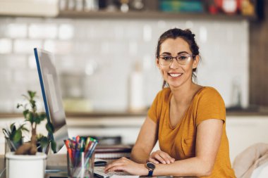 Evindeki stüdyoda bilgisayarla çalışan yaratıcı genç bir kadının portresi. Kameraya bakıyorum..