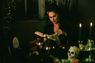 Çekici, olgun bir kadın Cadılar Bayramı partisi için koca bir kitap okuyor..