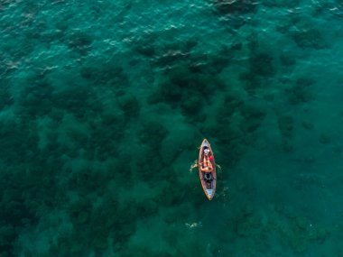 Yaz tatilinde berrak tropik deniz suyunda kanoyla kürek çekmekten hoşlanan tanınmayan bir adamın yüksek açılı çekimi..