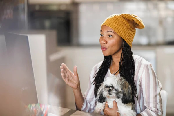 African woman developer having meeting online while working on computer at her home office, her pet dog is with her.