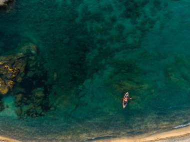 İyon Denizi 'nin berrak bir turkuaz suyunda kanoyla kürek çeken tanınmayan bir adamın yüksek açılı çekimi..