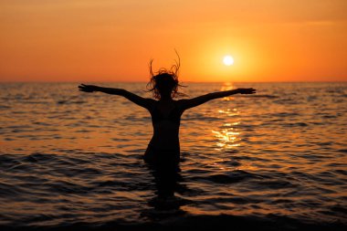 Çekici genç bir kadın gün batımında sahilde eğleniyor ve dinleniyor..