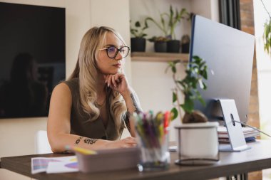 Genç bayan serbest tasarımcı ev ofisinden bilgisayarla uğraşırken düşünceli görünüyor..