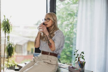Evinde rahat bir şekilde işten kahve molası verirken akıllı telefondan konuşan yaratıcı genç bir kadın..