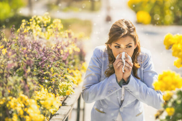 Shot of a young businesswoman blowing her nose with a tissue outside due to allergies or colds.