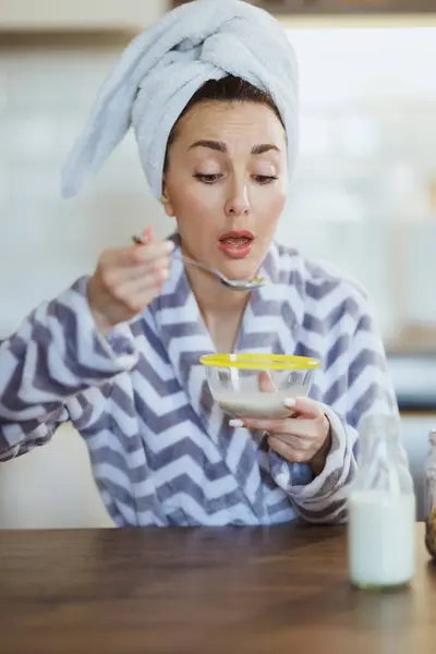 自宅のキッチンで朝食のためにインスタントオート麦を食べるバスローブの若い女性 — ストック写真