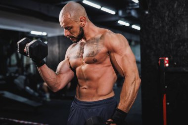 Spor salonunda dambılla ağır antrenman yapan kaslı bir vücut geliştiriciyi vurmuşlar. Pazularını ağırlıkla şişiriyor..